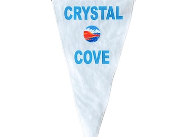 May include: White triangular pennant with blue text that reads "CRYSTAL COVE". A blue circle with a red and white sunset graphic is centered above the text.