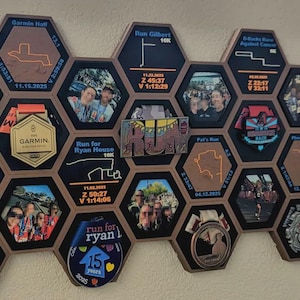 May include: A modular honeycomb wall display featuring hexagonal frames containing race medals, photographs, and engraved race details. The black and wood-toned frames showcase various running event memorabilia, including maps, dates, and finish times.