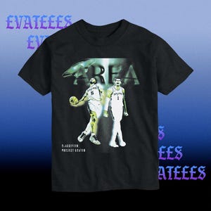K&ouml;nnte beinhalten: Schwarzes T-Shirt mit einer Grafik von zwei Basketballspielern in wei&szlig;en Trikots. Das Wort "AREA" ist &uuml;ber den Spielern aufgedruckt, darunter der Text "CLASSIFIED: PROJECT GREATER". Das T-Shirt hat einen blauen Farbverlauf im Hintergrund.