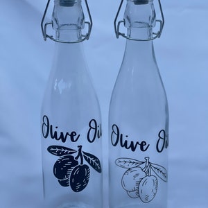 May include: Two clear glass bottles with silver swing top lids. Both bottles have black and white labels that say "Olive Oil" and feature a drawing of olives.