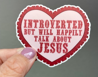 May include: A heart-shaped sticker with the text "INTROVERTED BUT WILL HAPPILY TALK ABOUT JESUS" in red letters. The sticker has a pink background and a red ruffled border. The sticker is held by a hand.