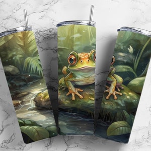 May include: Three stainless steel insulated tumblers with lids and straws. Each tumbler features a wraparound design of a frog in a jungle setting. The frog is green and yellow with large eyes. The background shows a stream and lush foliage.
