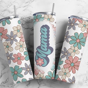 May include: Three stainless steel tumblers with a white background and a floral pattern in shades of blue, pink, and beige. One tumbler has the word "Mama" in a blue and white font with a small flower graphic.