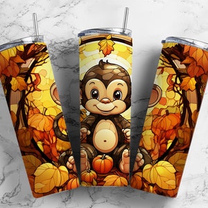 May include: Three stainless steel tumblers with a fall-themed design featuring a cartoon monkey holding a pumpkin. The tumblers have a clear lid and a straw.