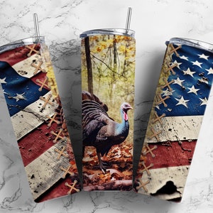 Può includere: Tre bicchieri in acciaio inossidabile con coperchi e cannucce. Due bicchieri presentano un design a bandiera americana invecchiata con dettagli cuciti. Il bicchiere centrale mostra un tacchino selvatico in un ambiente forestale. I bicchieri sono progettati per bevande fredde.