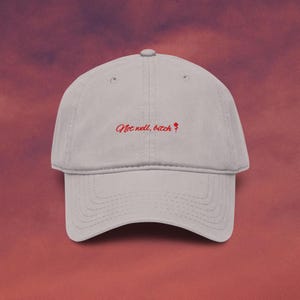 May include: A light gray baseball cap with the embroidered text "Not well, bitch" in red script. A small red rose graphic is next to the text. The cap has a curved brim and a fabric strap closure.