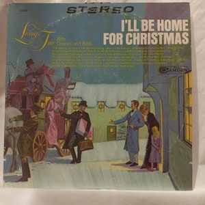 Puede incluir: Una portada de disco de vinilo vintage que muestra una escena de invierno nevada con un carruaje tirado por caballos y personas caminando. El título del álbum es "I'll Be Home For Christmas" con el subtítulo "With Chimes and Bells".