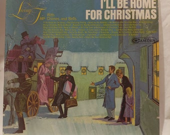 May include: A vintage vinyl record cover featuring a snowy winter scene with a horse-drawn carriage and people walking. The album title is "I'll Be Home For Christmas" with the subtitle "With Chimes and Bells".