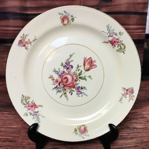 May include: A white ceramic dinner plate with a gold rim and a floral design. The flowers are pink, red, and purple, and they are arranged in a bouquet in the center of the plate. There are smaller floral designs around the edge of the plate.