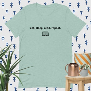 May include: A light blue t-shirt with the text "eat. sleep. read. repeat." and a black silhouette of an open book.