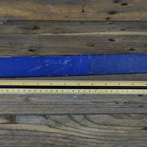 May include: A blue cardboard box with the word "МИШОЖ" written on it, and a wooden ruler with black and white markings.