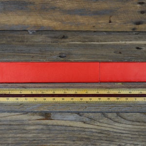 May include: A red, rectangular box containing a wooden ruler. The ruler is marked with numbers from 0 to 70.