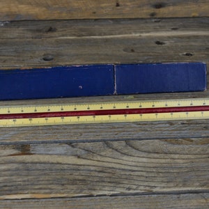 May include: A yellow and red ruler with markings in inches and centimetres. The ruler is lying on a wooden surface. The ruler is 30.5 centimetres long.