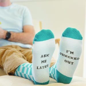 Peut inclure: Une paire de chaussettes rayées bleues et blanches avec le texte "Ask Me Later" sur une chaussette et "I'm Checked Out" sur l'autre chaussette.