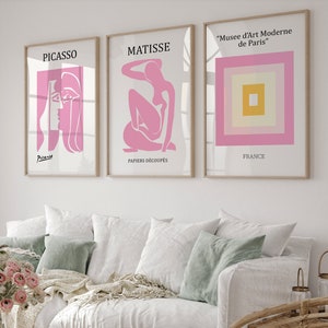 May include: Three framed art prints with pink and white designs. The prints feature the names "Picasso", "Matisse", and "Musée d'Art Moderne de Paris".