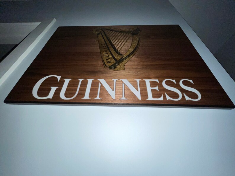 Pu&ograve; includere: Un cartello in legno con la parola "GUINNESS" in lettere bianche e un logo di arpa dorato con il testo "ESTD 1759".