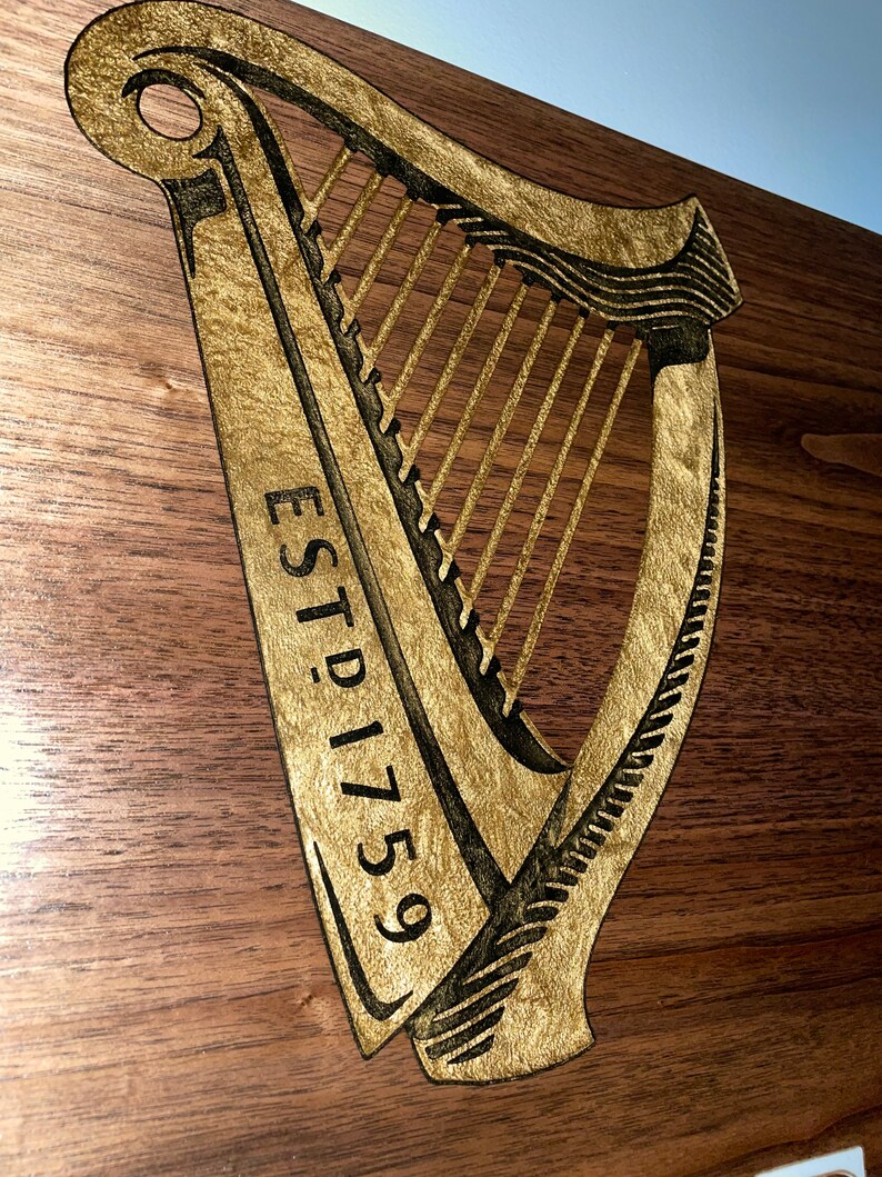 Pu&ograve; includere: Un cartello di legno con un'arpa dorata e il testo "ESTD 1759" inciso su di esso.