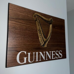Pu&ograve; includere: Un cartello di legno con un'arpa dorata e il testo "ESTD 1759" e "GUINNESS" in lettere bianche.