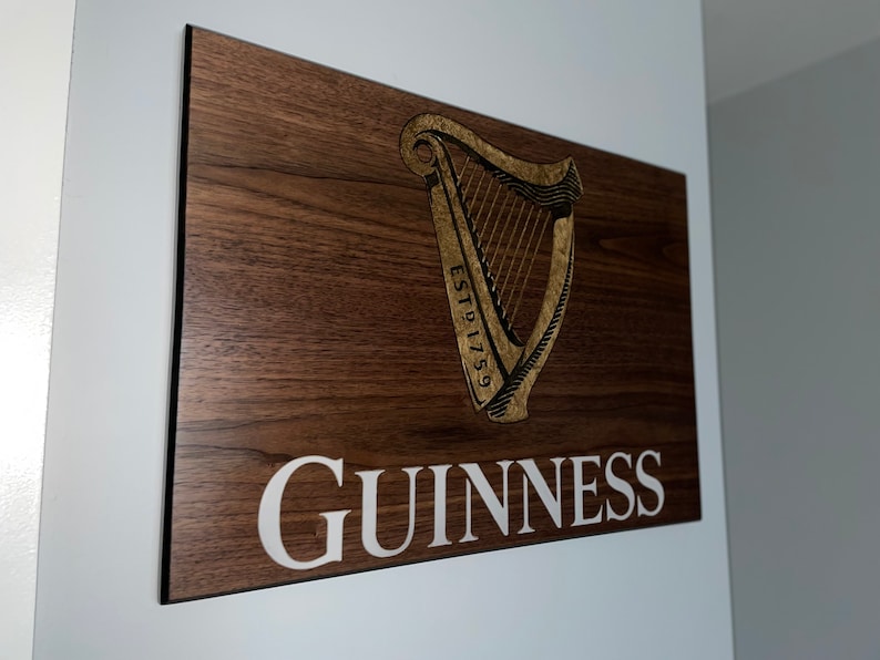 Pu&ograve; includere: Un cartello di legno con un'arpa dorata e il testo "ESTD 1759" e "GUINNESS" in lettere bianche.