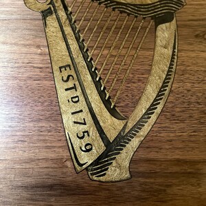 Pu&ograve; includere: Un cartello di legno con un'arpa dorata e il testo "ESTD 1759".
