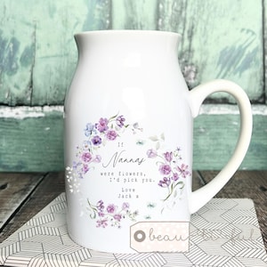 Könnte beinhalten: Weißer Keramikkrug mit gebogenem Griff, verziert mit einem floralen Kranz in Lila- und Blautönen. Der Text lautet: "Wenn Omas Blumen wären, würde ich dich pflücken. Liebe Jack x."