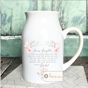 Puede incluir: Jarra de leche de cerámica blanca con asa, con un diseño floral y el texto "Bonus Daughter. I hope you always know just how amazing, loved and worthy you are. I may not have given you the gift of life, but I am so blessed & grateful that life gave me you. Love, Rachel"