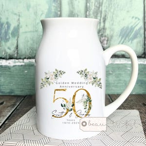 Puede incluir: Taza de cerámica blanca en forma de jarra de leche con un diseño floral dorado y el texto "Golden Wedding Anniversary 50 Scott & Jenny Years 1974-2024"