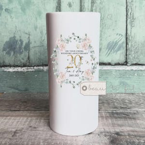 Könnte beinhalten: Eine weiße Keramikvase mit einem floralen Kranzdesign. Der Kranz enthält rosa Rosen und Grünzeug, umgeben von dem Text "ON YOUR CHINA WEDDING ANNIVERSARY" und "20th". Die Namen "Tom & Amy" und die Jahre "2005-2025" sind ebenfalls abgebildet.