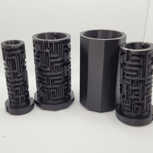 Op de afbeelding: Vier zwarte, 3D-geprinte cilindrische containers met een labyrintpatroon. De containers zijn van verschillende groottes en zijn in een rij gerangschikt van de kleinste tot de grootste.