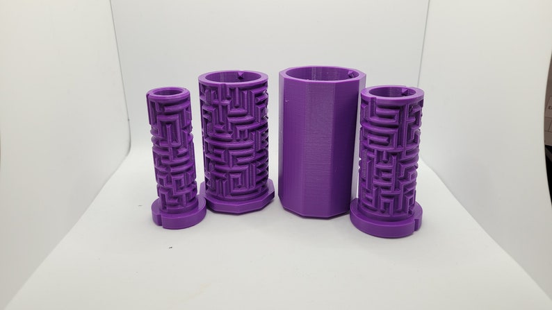 Op de afbeelding: Vier paarse 3D-geprinte cilindrische containers met een labyrintpatroon aan de zijkanten. De containers zijn van verschillende groottes en zijn in een rij gerangschikt.