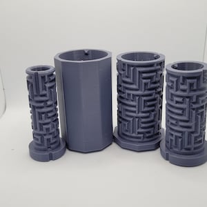 Op de afbeelding: Vier grijze 3D-geprinte cilinders met een labyrintpatroon. De cilinders zijn van verschillende grootte en zijn in een rij op een wit oppervlak gerangschikt.