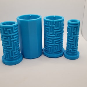 Op de afbeelding: Vier blauwe plastic mallen voor het maken van kaarsen. De mallen zijn cilindrisch en hebben een labyrintpatroon aan de buitenkant.