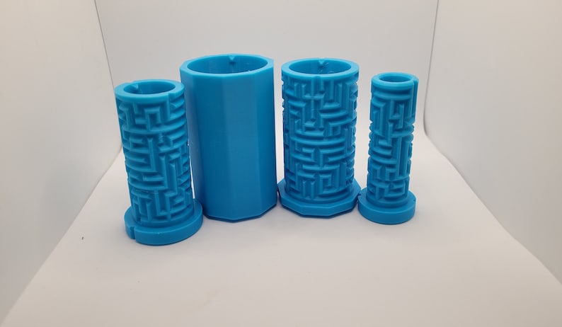 Op de afbeelding: Vier blauwe plastic mallen voor het maken van kaarsen. De mallen zijn cilindrisch en hebben een labyrintpatroon aan de buitenkant.