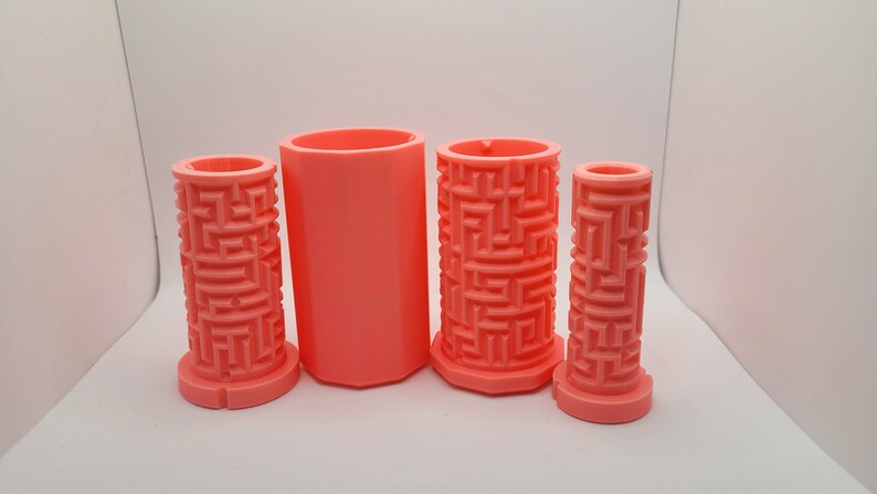Op de afbeelding: Vier roze plastic mallen voor het maken van kaarsen. De mallen zijn cilindrisch en hebben een labyrintpatroon aan de buitenkant.