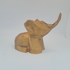 May include: A small, wooden elephant sculpture with a geometric design. The elephant is painted in a gold colour and has a raised trunk.