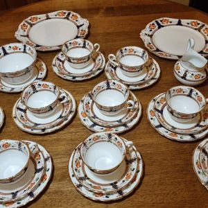 Könnte beinhalten: Eine weiße Keramik-Tasse mit schwarzem Henkel und dem Text "But First, Coffee" in fetter, schwarzer Schrift. Die Tasse steht vor einem verschwommenen Hintergrund. Die Tasse ist etwa 10 cm hoch.