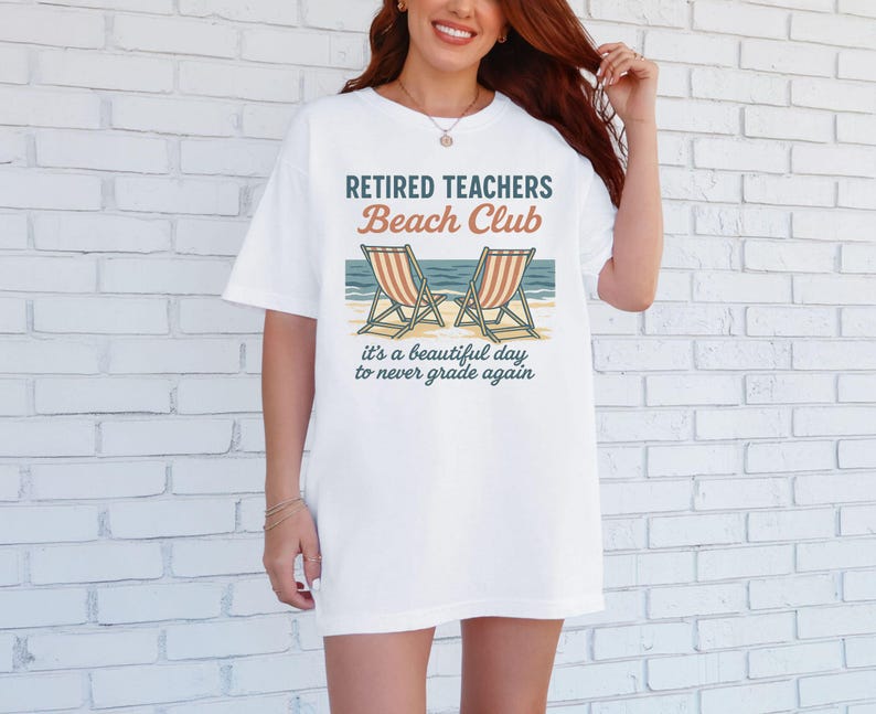 May include: White t-shirt with the text "Retired Teachers Beach Club" and a graphic of two beach chairs. The text below the graphic reads "It's a beautiful day to never grade again."