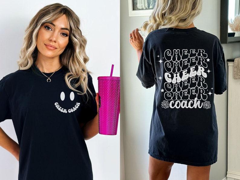 Peut inclure: T-shirt noir avec un smiley blanc et le texte "Cheer Coach" sur le devant. Le dos du t-shirt porte le texte "Cheer" r&eacute;p&eacute;t&eacute; cinq fois dans une police r&eacute;tro, avec le mot "Coach" au centre.