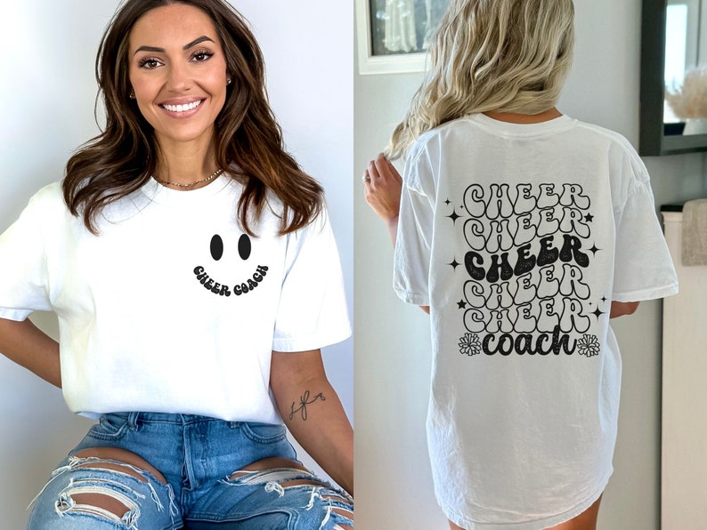 Peut inclure: T-shirt blanc avec un smiley noir et le texte "Cheer Coach" sur le devant. Le dos du t-shirt porte le texte "Cheer" r&eacute;p&eacute;t&eacute; cinq fois dans une police r&eacute;tro, suivi de "Coach" avec une fleur de chaque c&ocirc;t&eacute;.