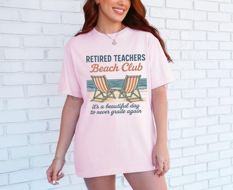 May include: Pink t-shirt with the text "Retired Teachers Beach Club" and a graphic of two beach chairs. The text below the graphic reads "It's a beautiful day to never grade again."