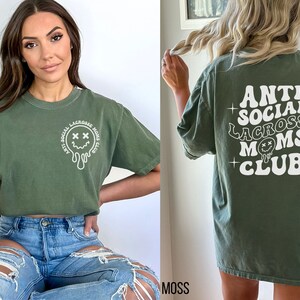 May include: Green t-shirt with a white graphic that says "Anti Social Lacrosse Moms Club" and a melting smiley face.