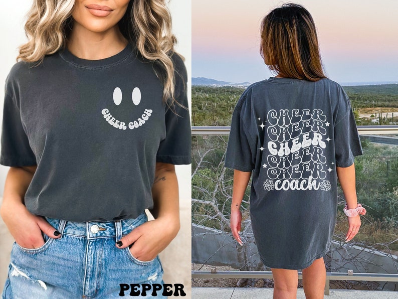 Peut inclure: Deux femmes portant des t-shirts gris fonc&eacute; avec du texte blanc. Le t-shirt de gauche a un smiley et le texte "Cheer Coach". Le t-shirt de droite a le texte "Cheer" r&eacute;p&eacute;t&eacute; cinq fois et "Coach" en bas.