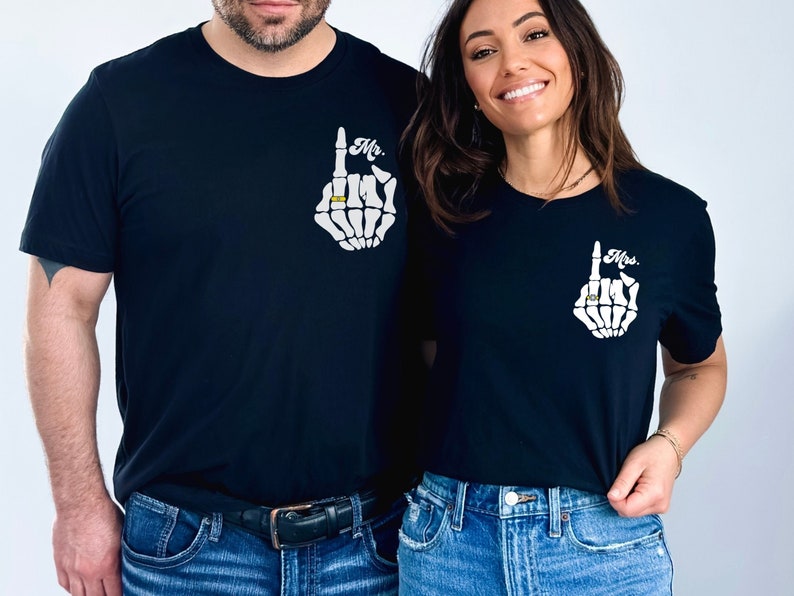 Pode incluir: Um casal vestindo camisetas pretas combinando com um design de m&atilde;o de esqueleto e as palavras "Mr." e "Mrs." impressas nelas. A m&atilde;o de esqueleto est&aacute; usando um anel no dedo indicador.