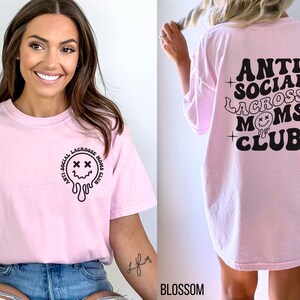 May include: Pink t-shirt with a black graphic that says "Anti-Social Lacrosse Moms Club" and a dripping smiley face with X's for eyes. The back of the shirt has the same graphic but without the smiley face.