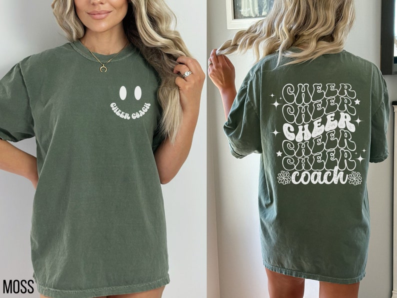Peut inclure: Un t-shirt vert avec un smiley blanc et le texte "Cheer Coach" sur le devant. Le dos du t-shirt a le texte "Cheer Coach" r&eacute;p&eacute;t&eacute; cinq fois dans une police r&eacute;tro avec des &eacute;toiles et des fleurs.