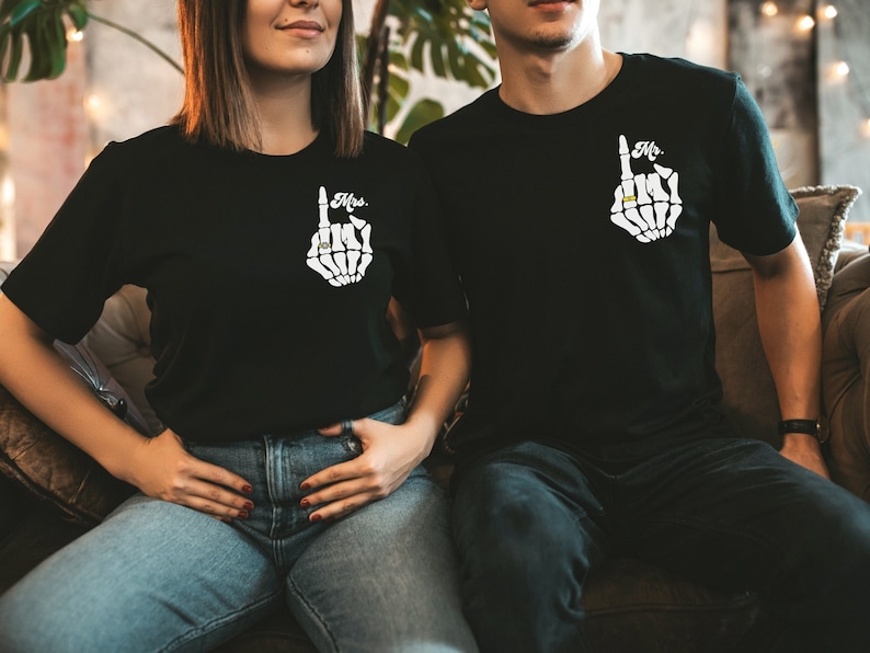 Pode incluir: Um casal vestindo camisetas pretas combinando com um gr&aacute;fico de m&atilde;o de esqueleto e as palavras "Mr." e "Mrs." impressas nelas.