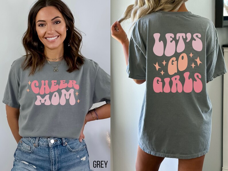 May include: A grey t-shirt with a pink and orange retro-style graphic that says "Cheer Mom" on the front and "Let's Go Girls" on the back.