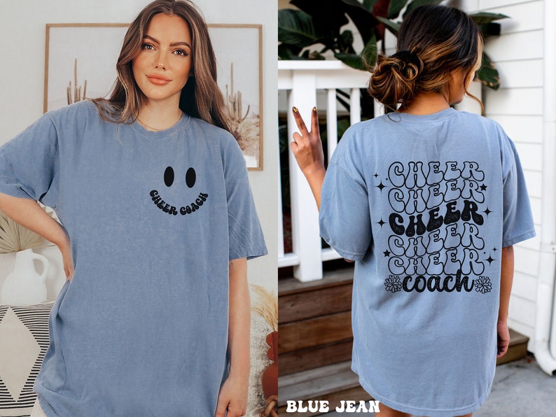 Peut inclure: Un t-shirt bleu avec un visage souriant et le texte "Cheer Coach" sur le devant. Le dos du t-shirt porte le texte "Cheer" r&eacute;p&eacute;t&eacute; cinq fois dans une police r&eacute;tro avec un motif de fleurs et d'&eacute;toiles.