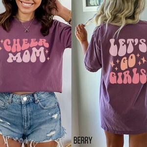 May include: Purple t-shirt with a pink and orange graphic that says "Cheer Mom" on the front and "Let's Go Girls" on the back.