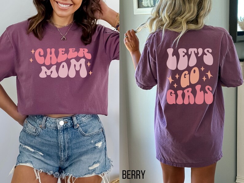 May include: Purple t-shirt with a pink and orange graphic that says "Cheer Mom" on the front and "Let's Go Girls" on the back.